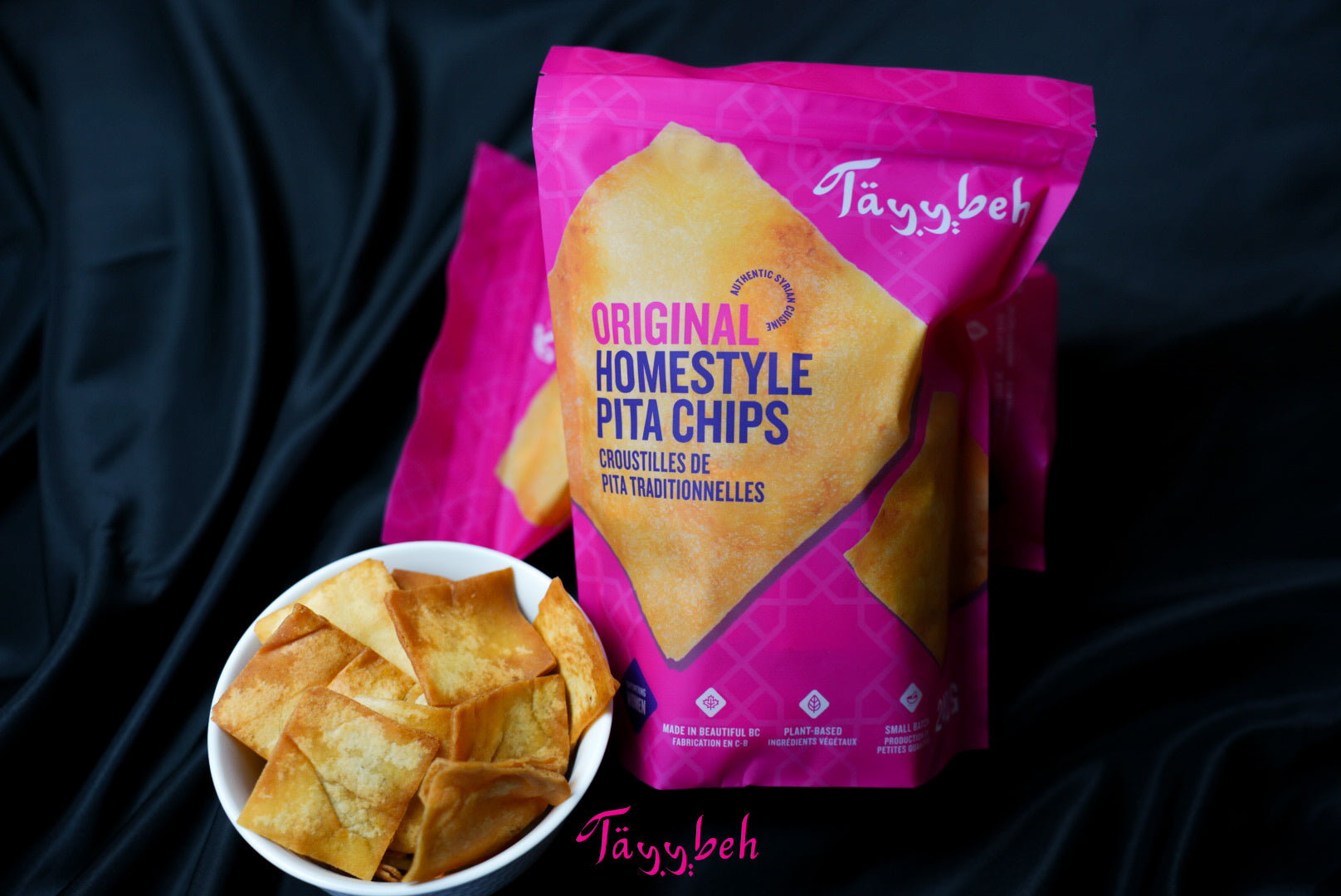 Homestyle pita chips by Tayybeh, nut-free and vegan, placed alongside a bowl of the same on a pink background.