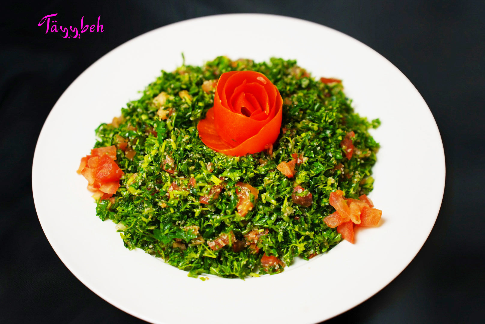 A vibrant Tayybeh Tabbouleh salad with a rose-shaped tomato centerpiece, surrounded by small tomato pieces and hearty bulgur wheat.