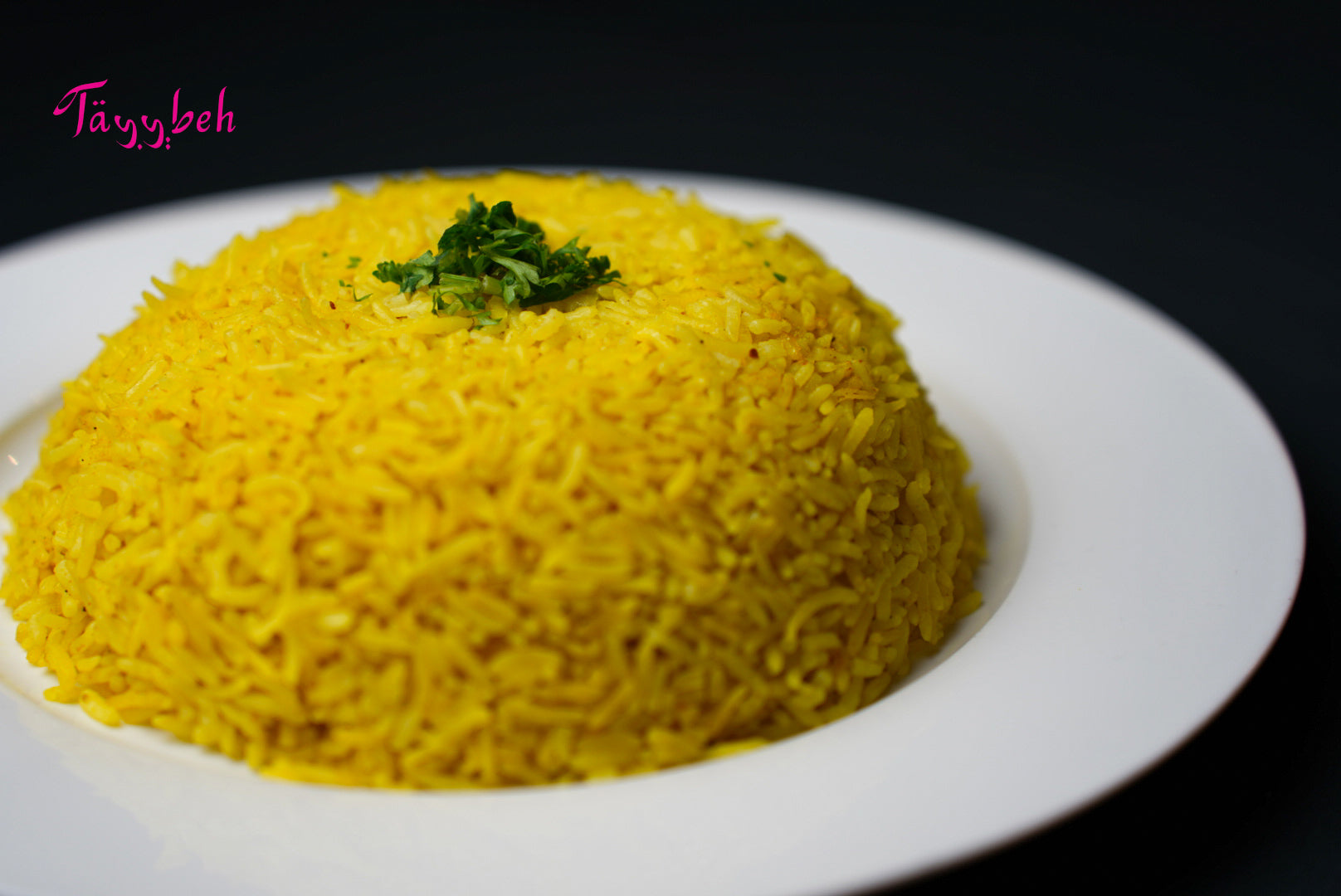 A plate of Tayybeh's flavorful Mandi Rice, expertly garnished with fresh green herbs, served on a white dish against a dark background.