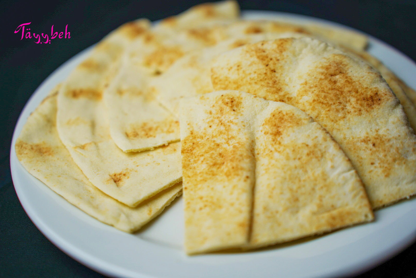 A plate featuring Tayybeh's Pita Bread, with two pieces cut into triangles and slightly overlapping, serves as an ideal side dish.