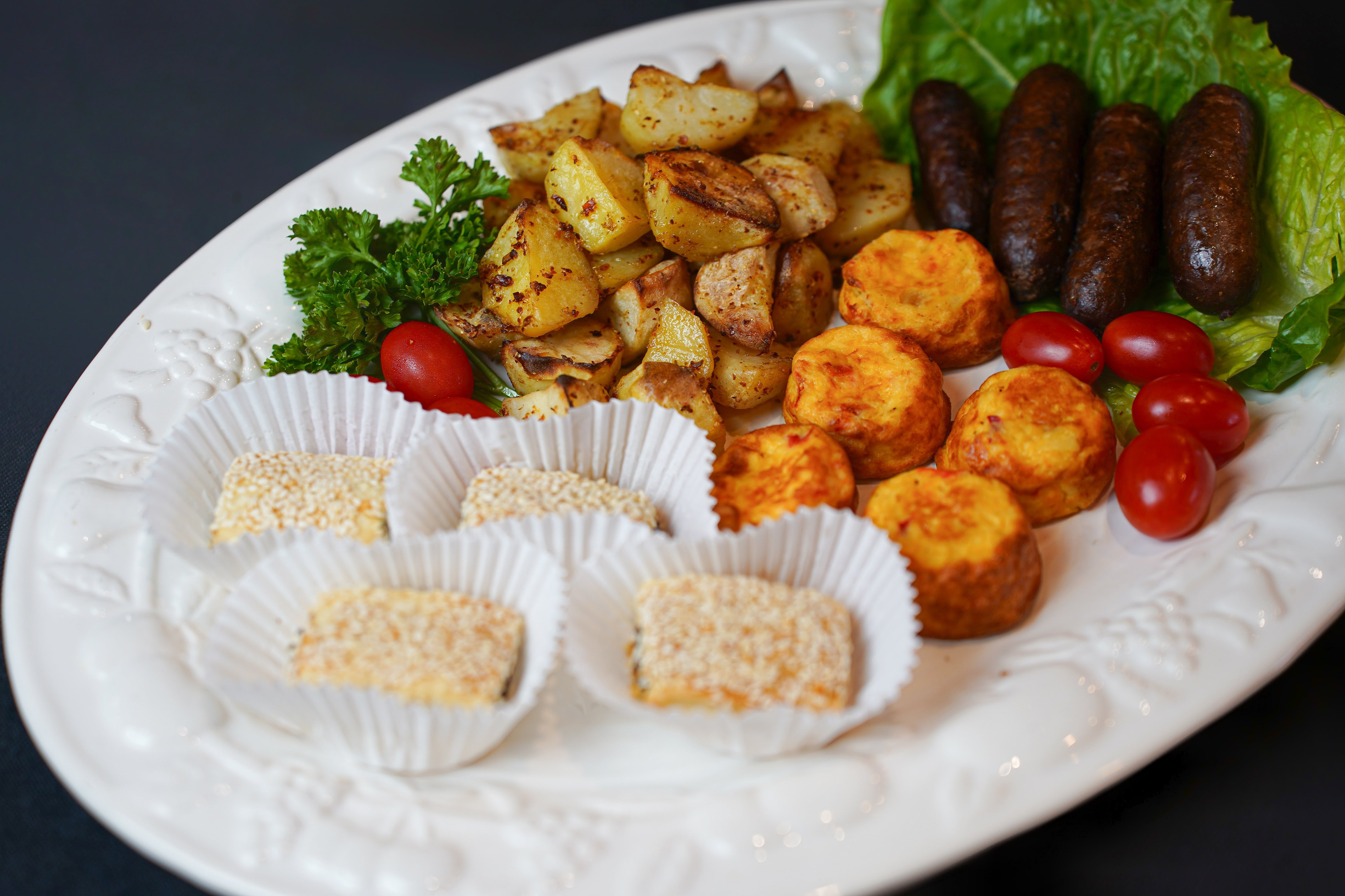 A platter from Tayybeh's Hot Breakfast features roasted potatoes, sausages, gluten-free cheddar biscuits, cherry tomatoes, sesame cookies, and leafy greens.