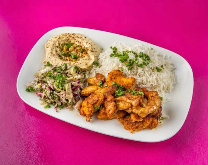 A plate of Tayybeh's Chicken Shawerma Meal, showcasing grilled chicken strips, basmati rice, creamy hummus, and salad adorned with parsley, is placed against a vibrant pink background.