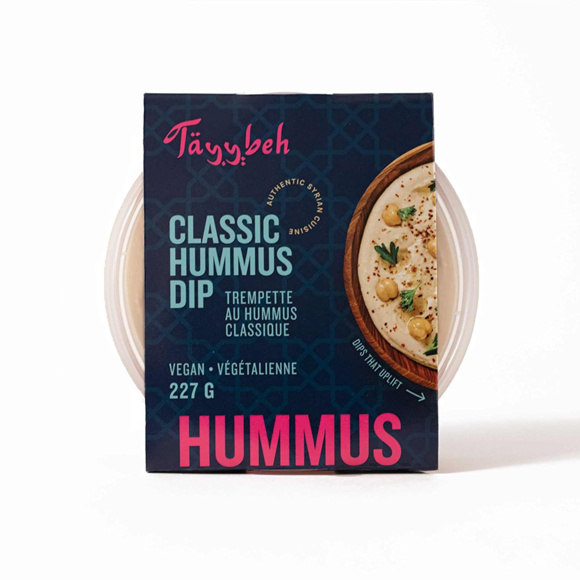 A 227g container of Tayybeh's Classic Hummus Dip showcases rich chickpeas and creamy tahini sauce, beautifully garnished with parsley, and prominently labeled as vegan.