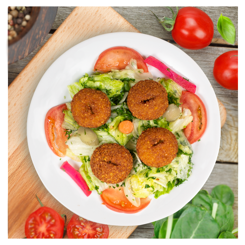 Introducing the "Falafel Salad" by Tayybeh: A vibrant plate of lettuce, tomatoes, and pickles featuring four crispy chickpea falafel balls, all drizzled with creamy tahini sauce and surrounded by fresh vegetables on a wooden surface.