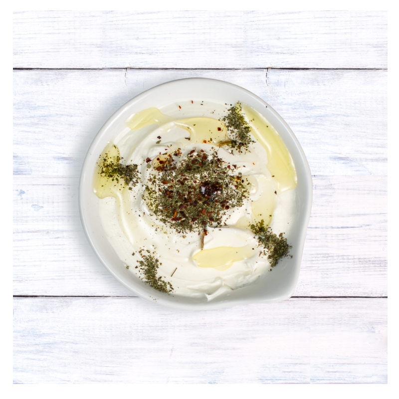 A serving from the Tayybeh Labneh dip pack, enhanced with mint, olive oil, herbs, and spices, presented on a light wooden surface.