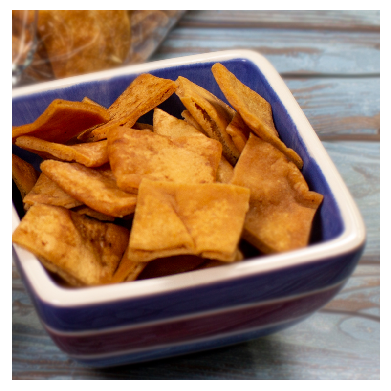 A small square bowl filled with crispy, golden-brown Tayybeh Pita Chips, set on a wooden table surface.