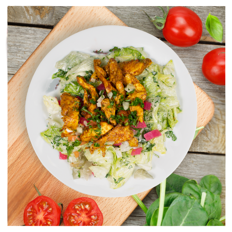 A Shawerma Salad by Tayybeh, featuring a plate of vibrant greens with grilled chicken, accompanied by fresh tomatoes and spinach leaves, all enhanced with a zesty lemon olive oil vinaigrette and elegantly arranged on a wooden board.