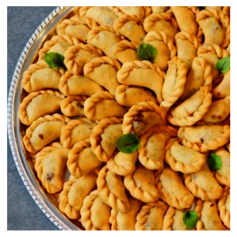 A plate filled with neatly arranged Damascus Delights fried dumplings garnished with small green mint leaves, perfectly paired with a side of Mhammara dip from Tayybeh.