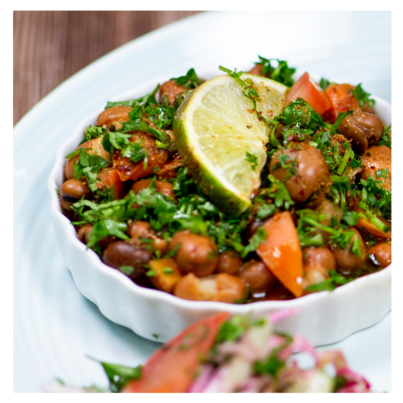 A serving of Tayybeh's Fava Bean Stew Meal, garnished with chopped tomatoes, cilantro, and a slice of lime, pairs perfectly with warm pita bread.