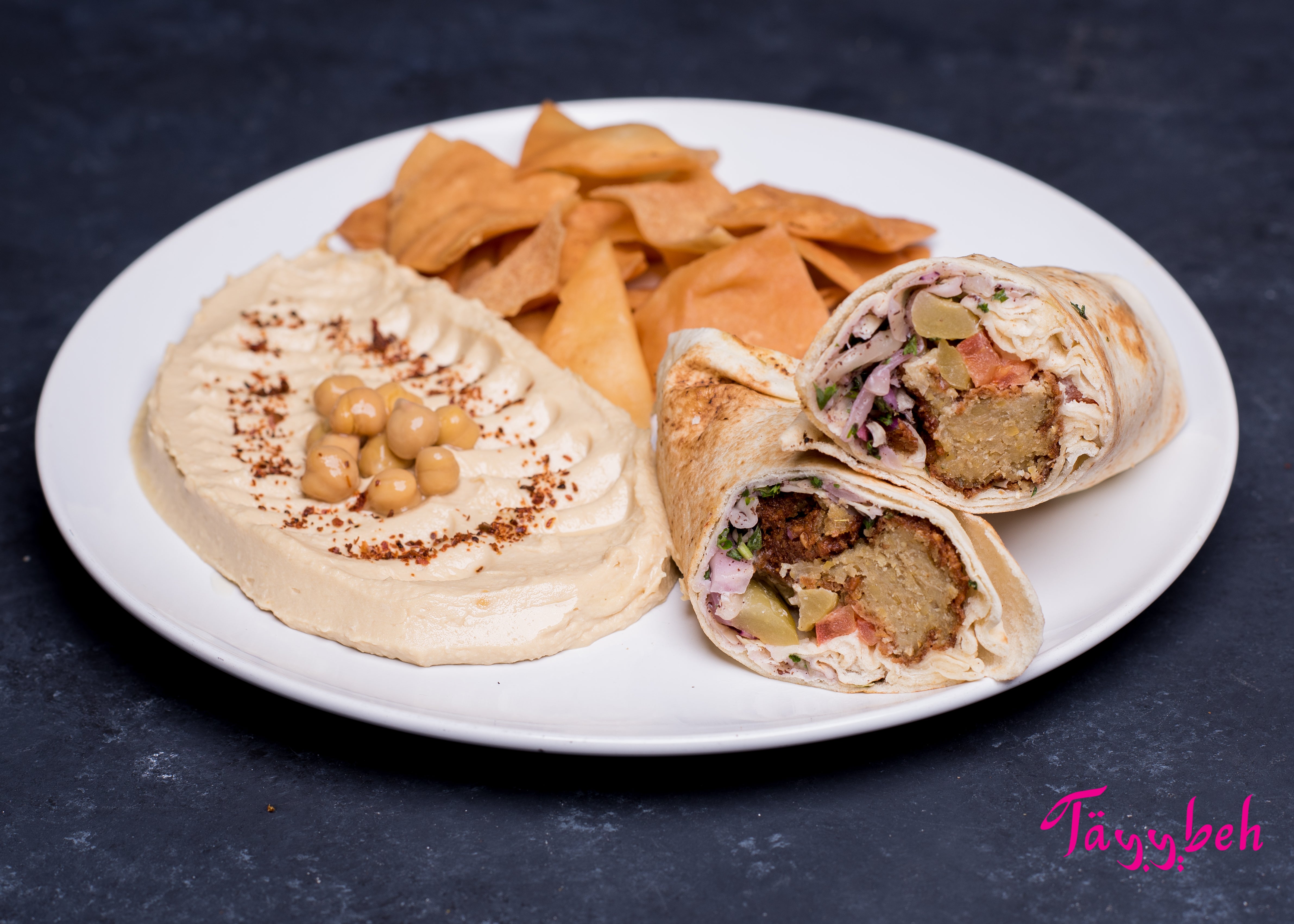 Enjoy the Falafel Wrap Combo from Tayybeh, which includes a delightful hummus dip topped with whole chickpeas, crispy pita chips, and a sliced pita wrap filled with falafel and fresh vegetables.