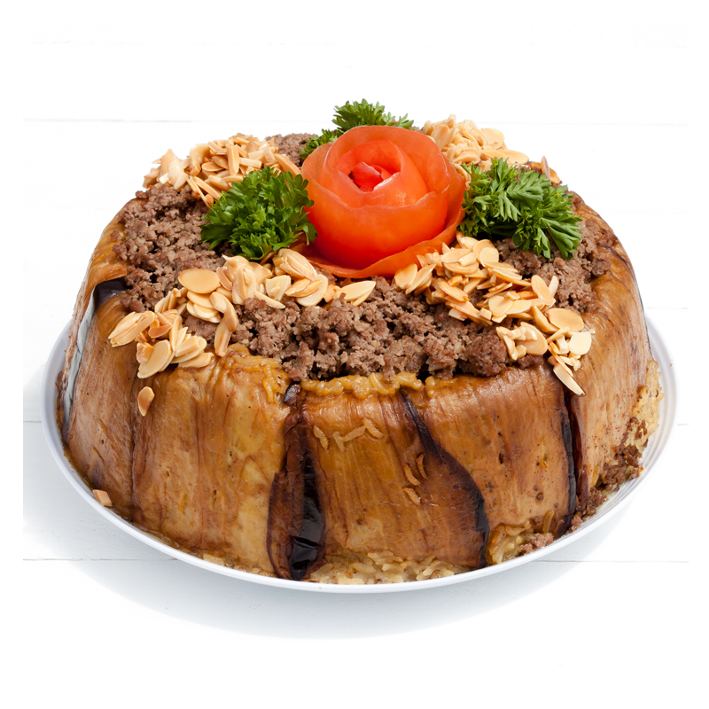 The dish, Makloubeh by Tayybeh, is an enticing gluten-free creation featuring slow-cooked aromatic rice crowned with seasoned ground meat, almond slices, and a tomato rose garnish. It is elegantly arranged on a white plate and artfully bordered with eggplant slices and parsley accents for a delightful presentation.