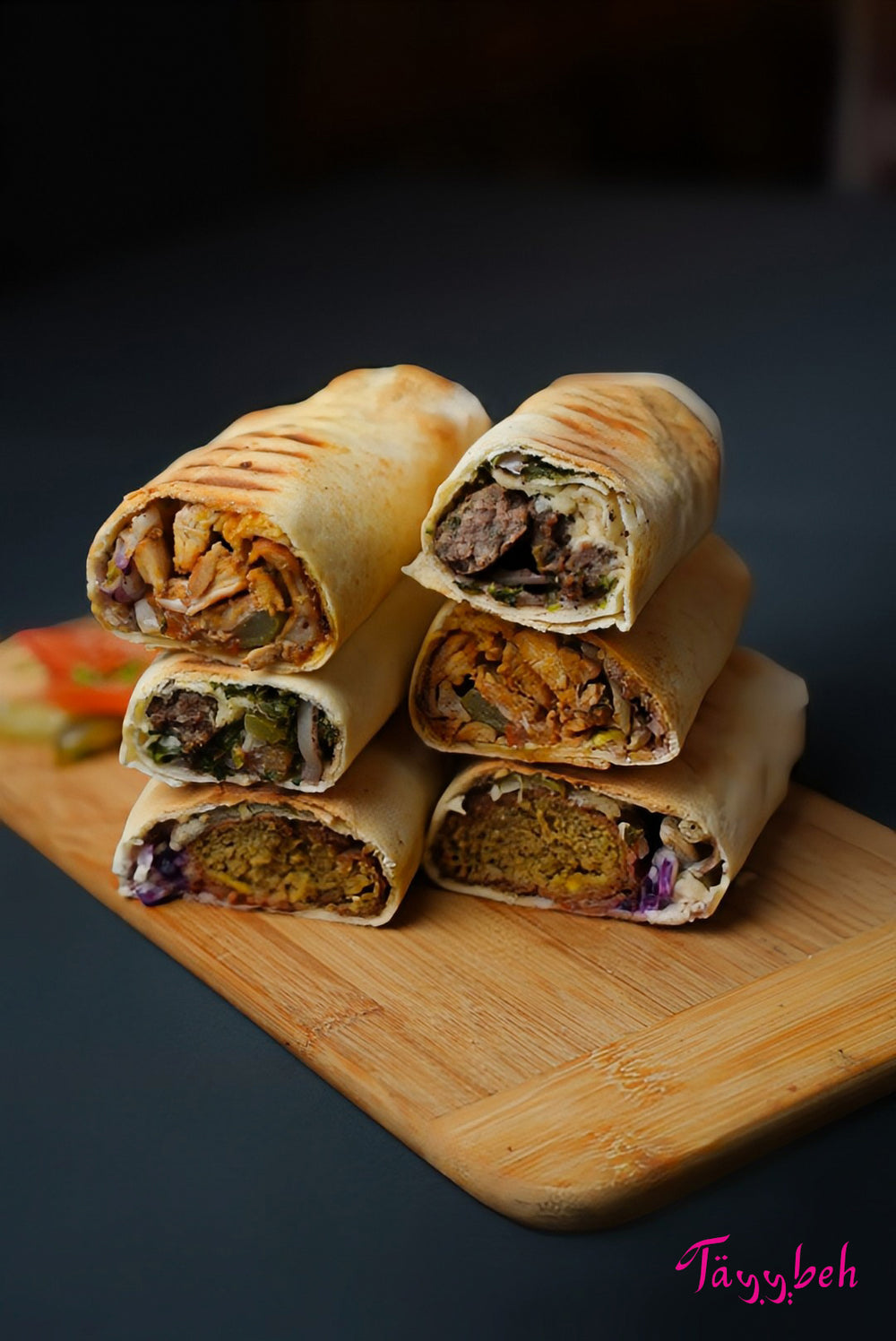 A collection of five assorted wraps, featuring the savory Chicken Shawarma Wrap and the flavorful Falafel Wrap, rests on a wooden board, filled with various ingredients like meat and vegetables from Tayybeh's Assorted Syrian Wrap Platter.