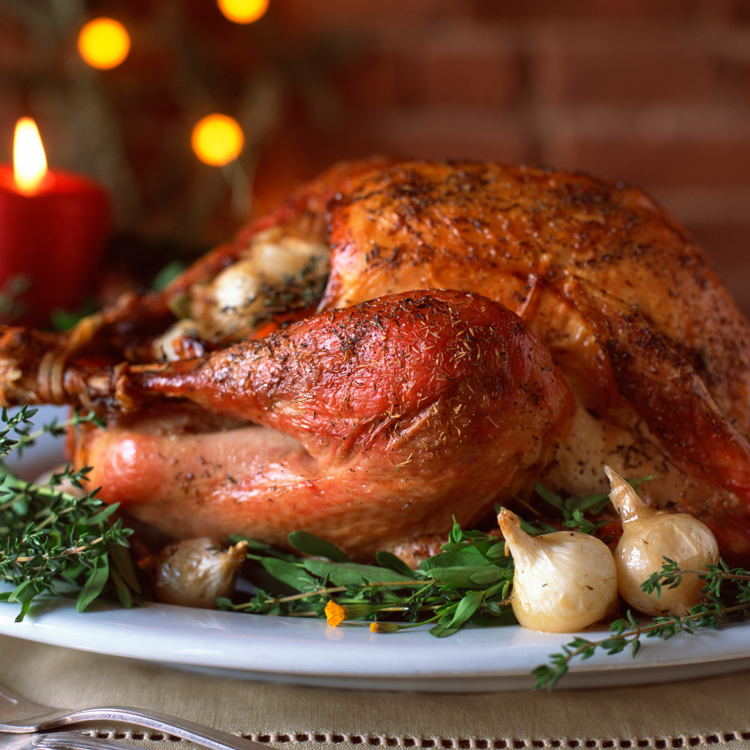 The Holiday Menu platter from Tayybeh showcases a beautifully garnished turkey with herbs and roasted onions, illuminated by the warm glow of a lit candle in the background.